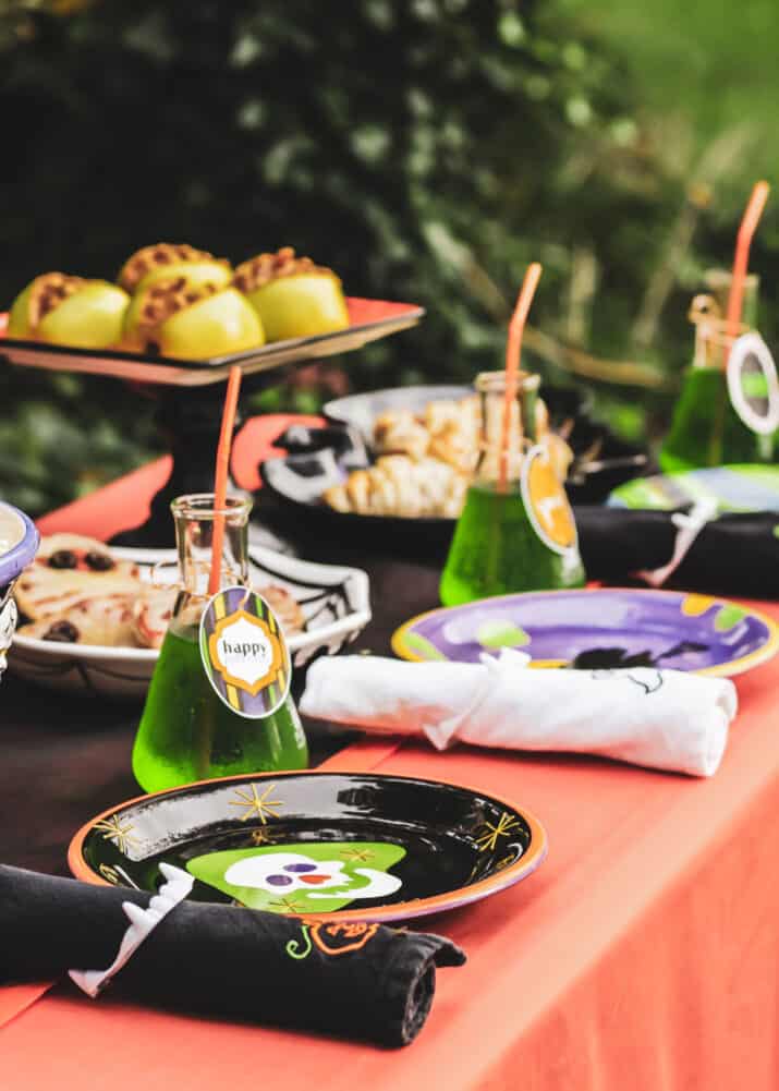 Halloween table with food platters, plates and drinks on top.