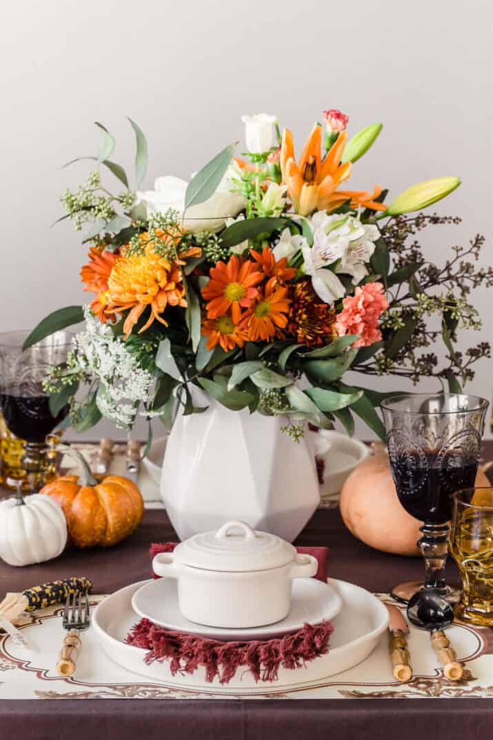 fall place setting with white plates and bowl on brown table cloth and fall flowers centerpiece