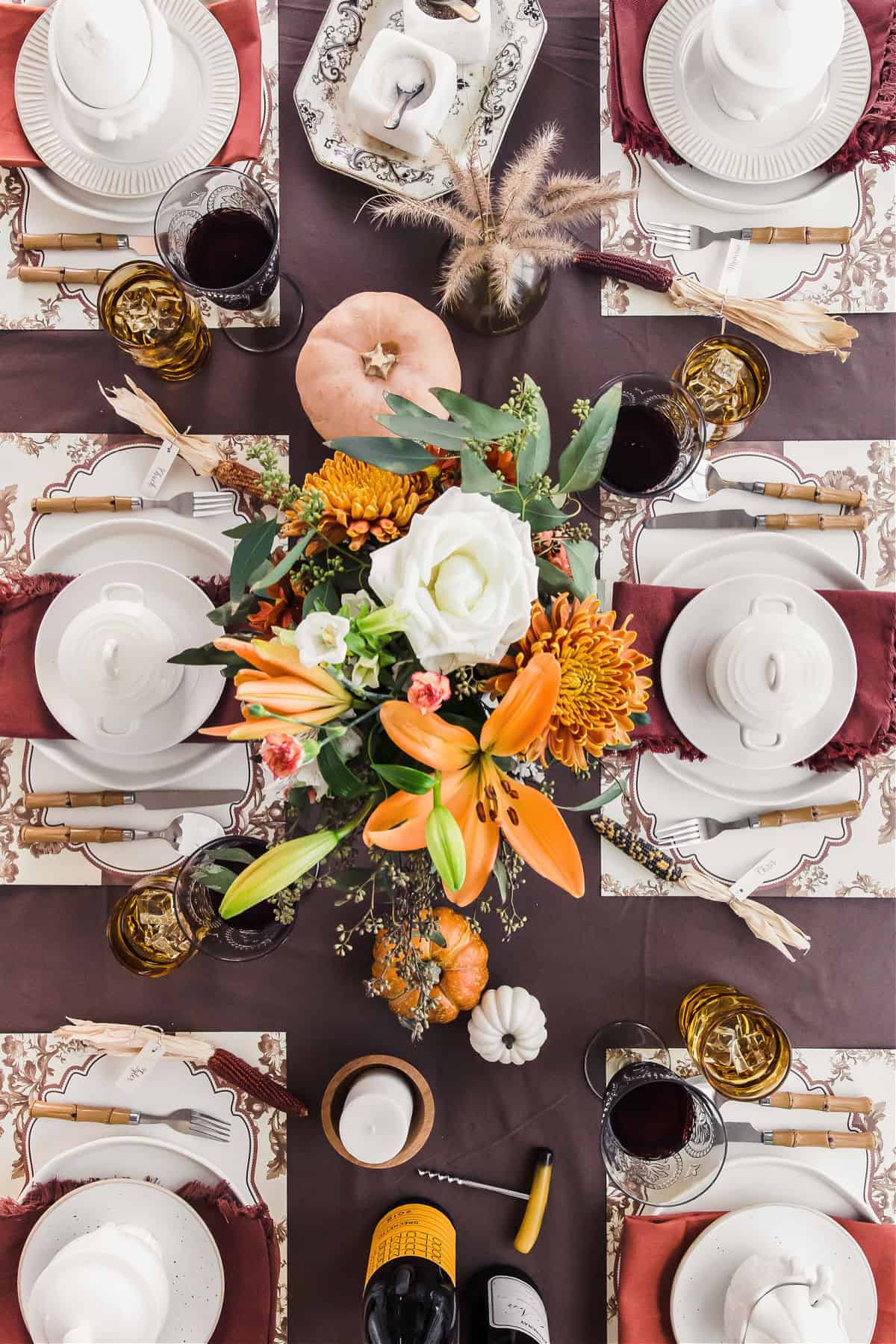 thanksgiving table setting overhead view with white plates and bowls on brown tablecloth and flower centerpiece