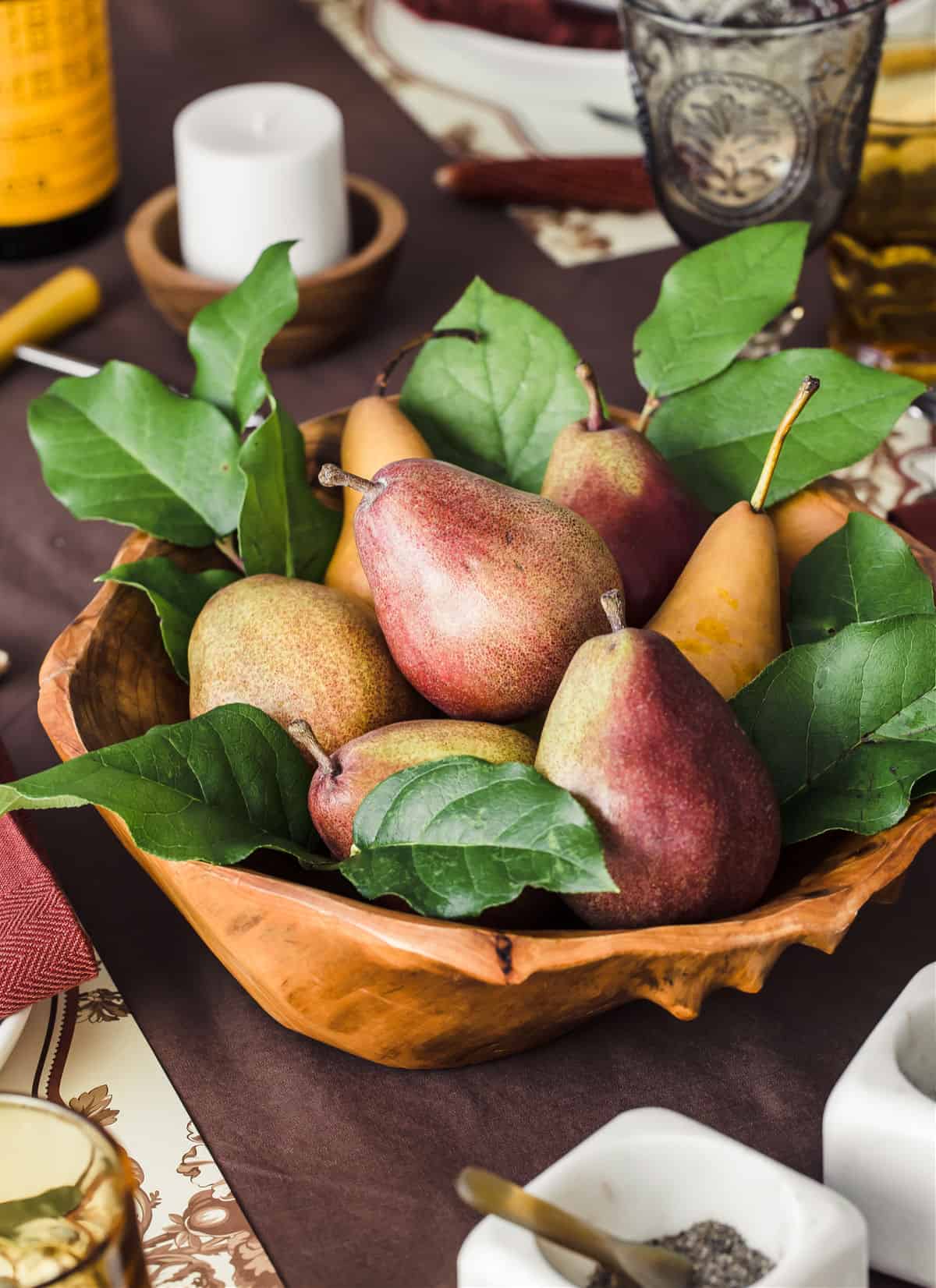 pears in wood bowl surrounded by green leaves, on brown table