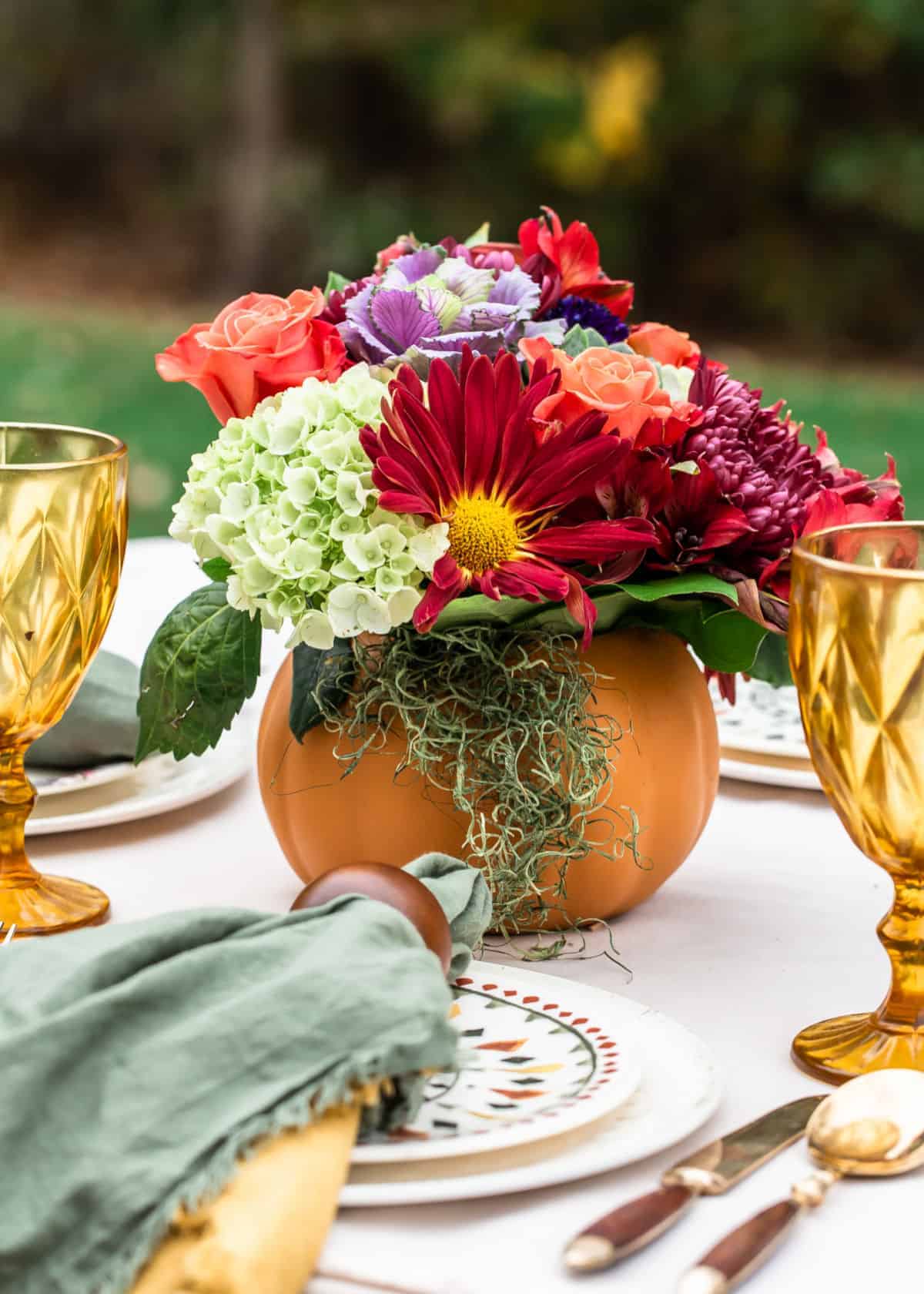 fall flowers in pumpkin vase on dining table outdoors