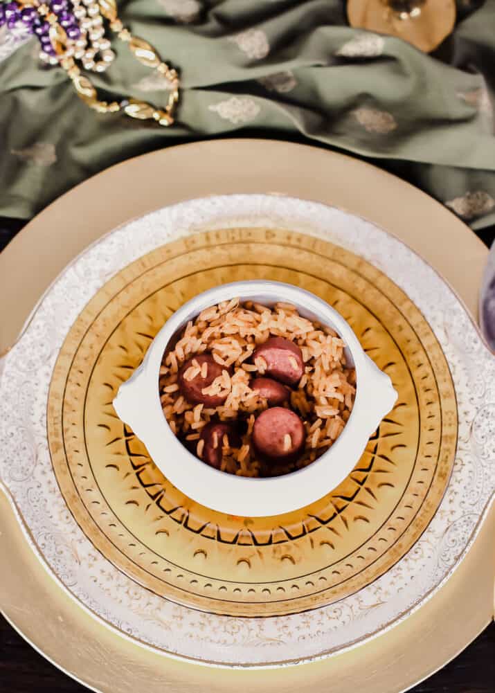 sausage and rice in white bowl sitting on gold plates on dinner table.
