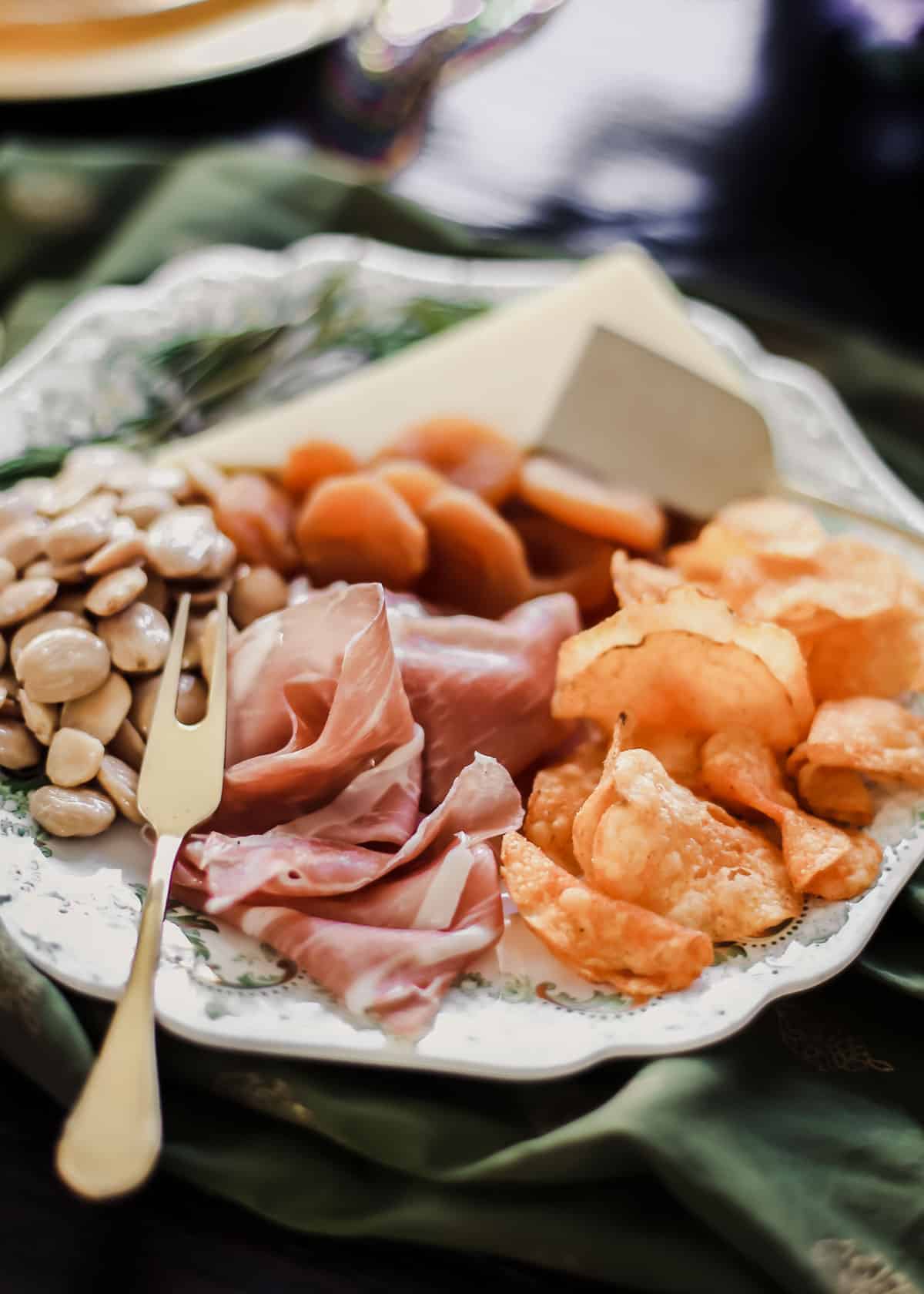 small plate filled with almonds, prosciutto, cheese, dried apricots and potato chips.