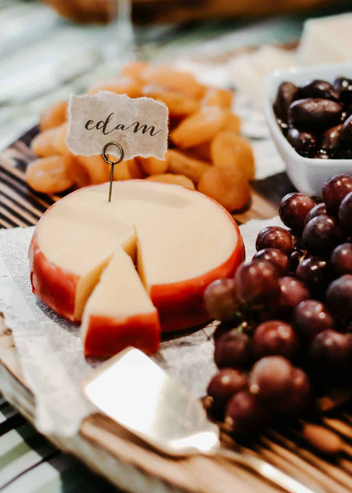 round block of Edam cheese with DIY label attached, with grapes and dried apricots.
