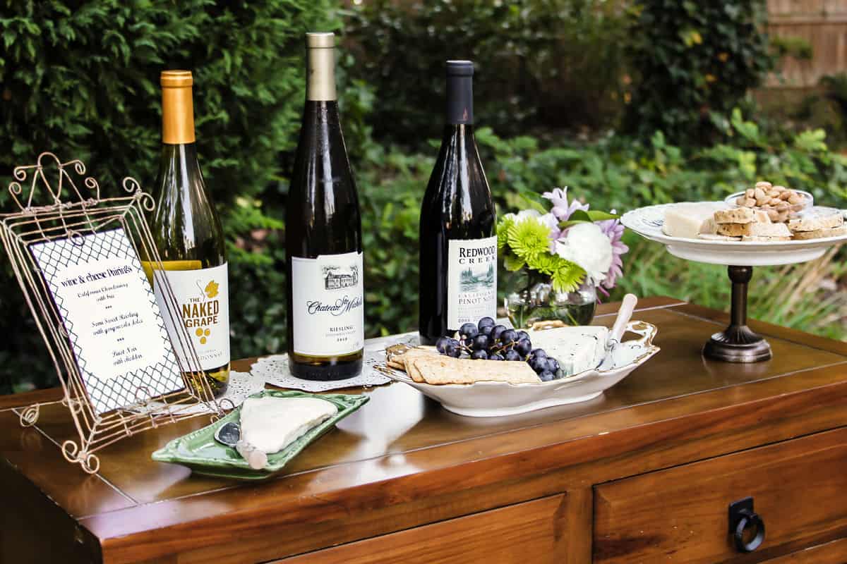 table set up outdoors with 3 wine bottles and 3 cheeses to pair with them.