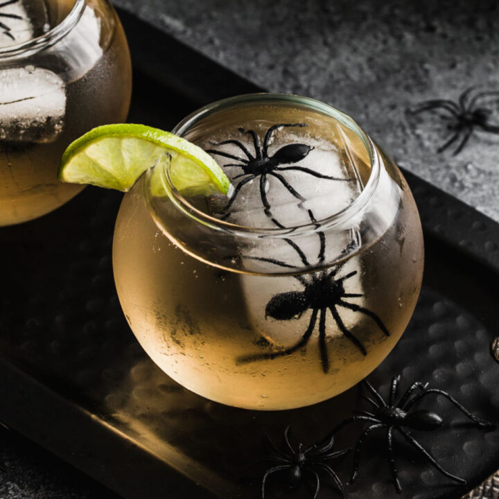 round glass with drink inside and spider ice cubes.