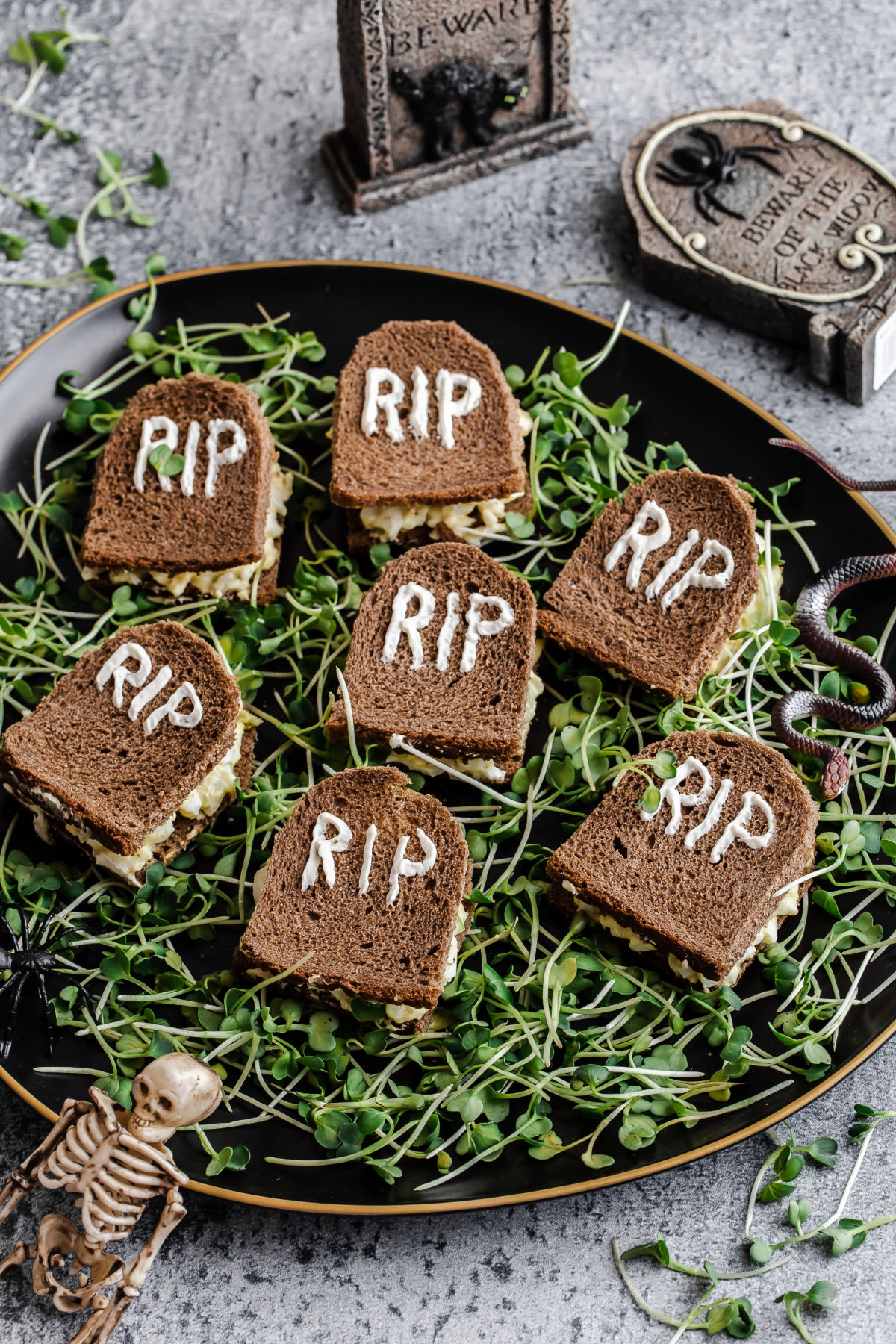 small sandwiches cut to look like Halloween tombstones, laying on a bed of microgreens.