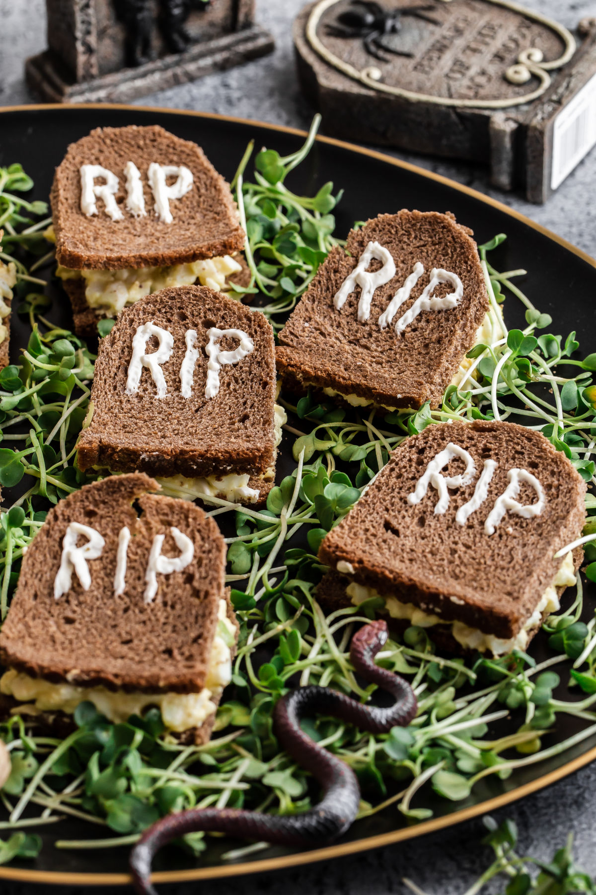 small sandwiches cut to look like Halloween tombstones, laying on a bed of microgreens.