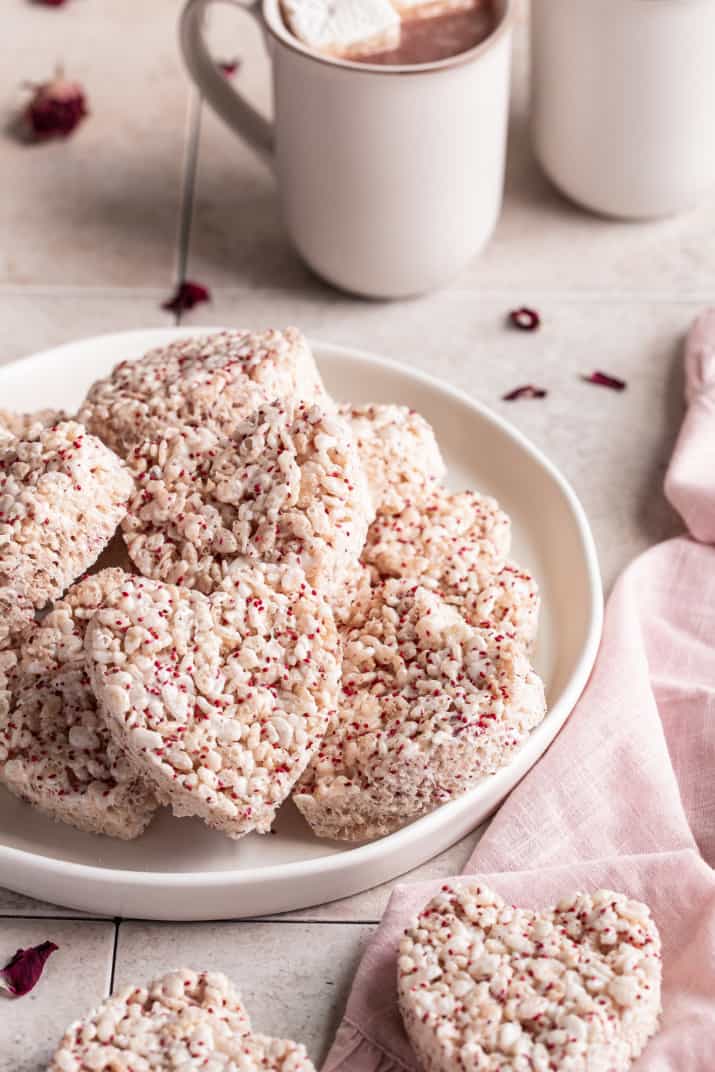 heart shaped cutout rice krispie treats on plate with mugs of hot cocoa