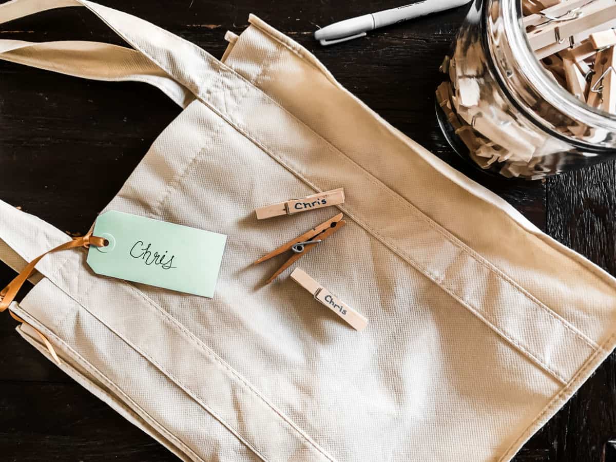 reusable shopping tote with name tag tied on, and clothespins in a jar on the side.