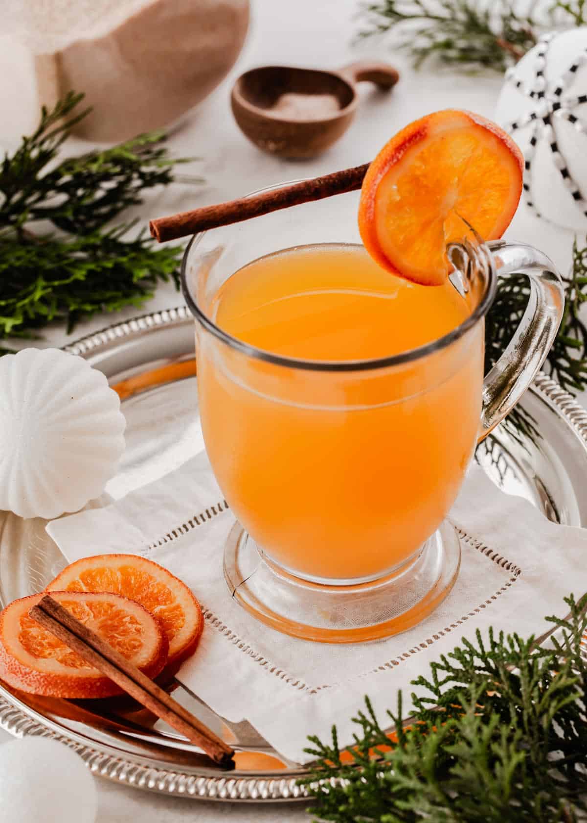 orange drink in glass mug garnished with cinnamon stick and orange wheel.