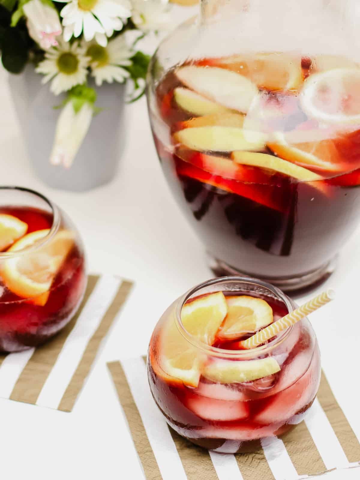two small glasses and a pitcher filled with sangria and fruit.