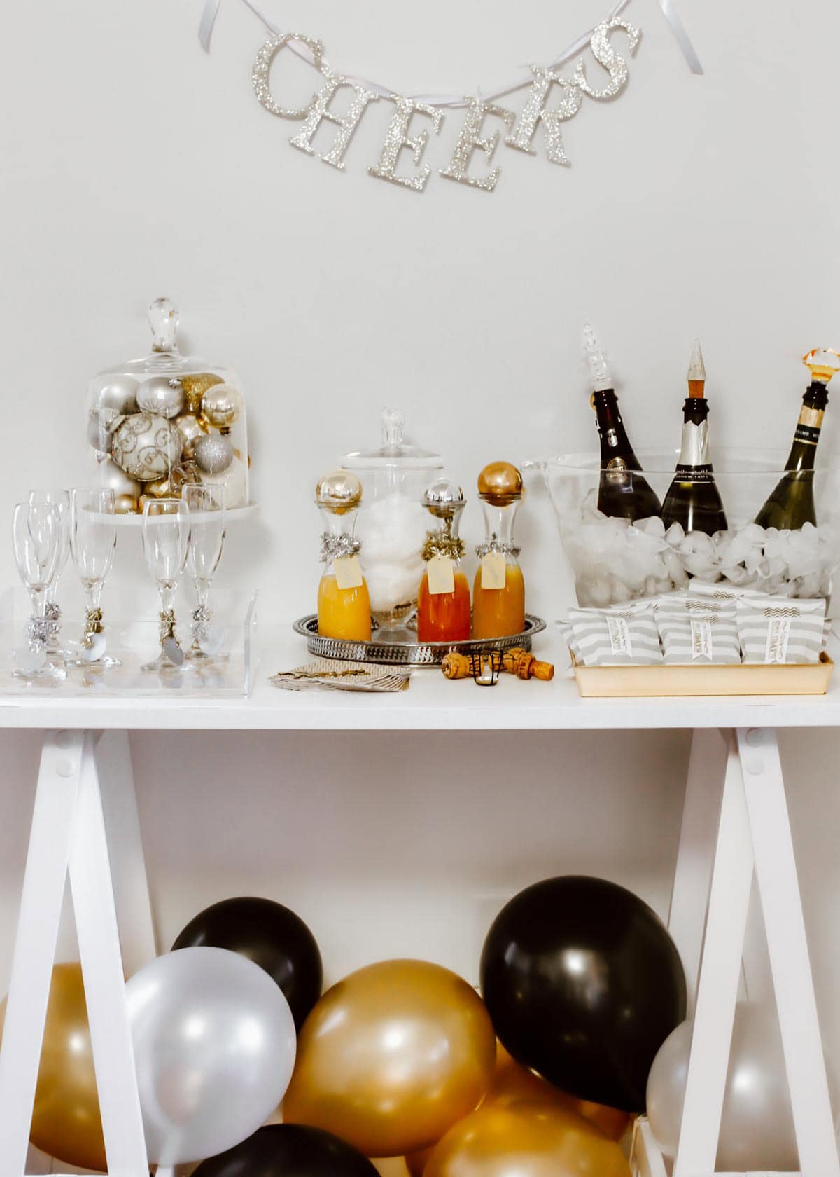 holiday champagne bar with balloons, bottles in ice tub, and juice for mimosas.