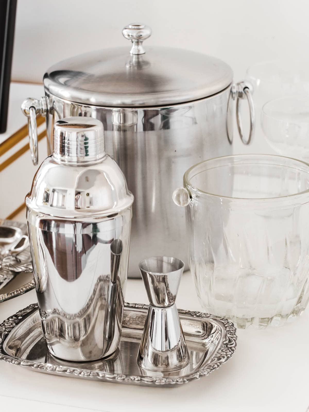 silver ice bucket, shaker and jigger on white table.