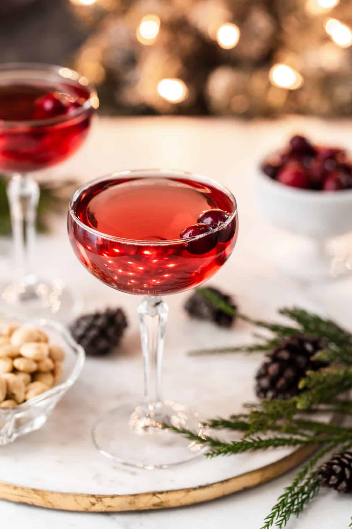 red drink in coupe glass on white tray with Christmas tree in background
