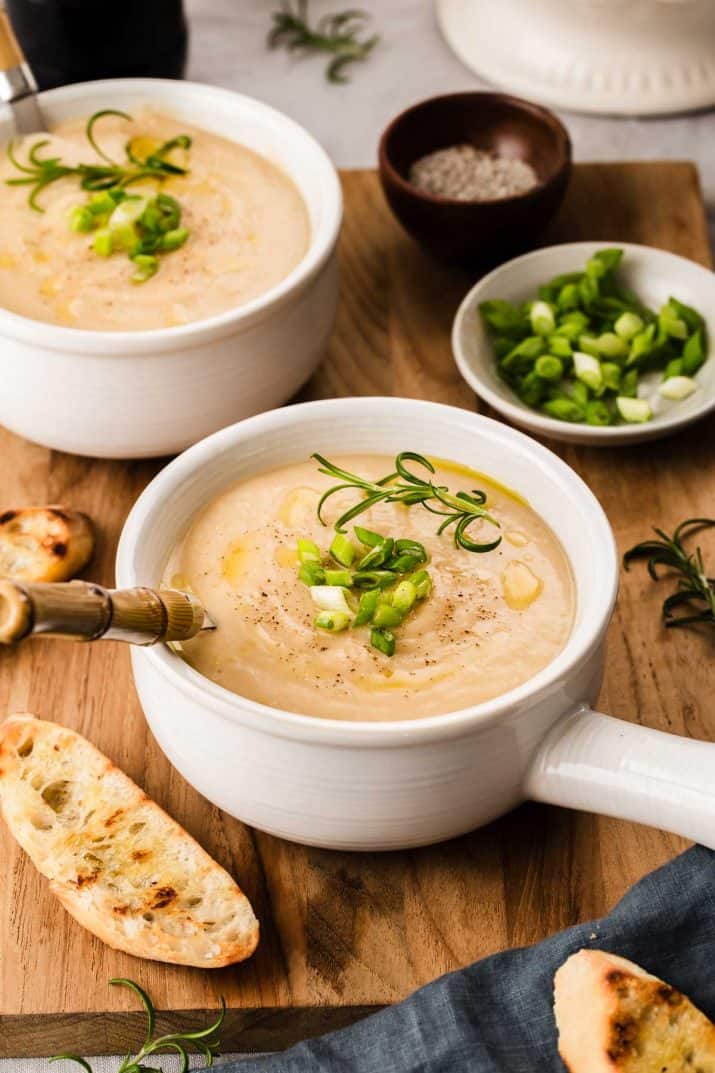 smooth white soup in white bowls, sitting on wood board with crostini bread.