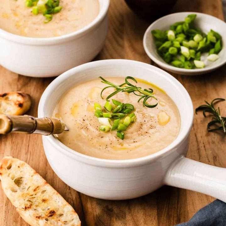 smooth white soup in white bowls, sitting on wood board with crostini bread.