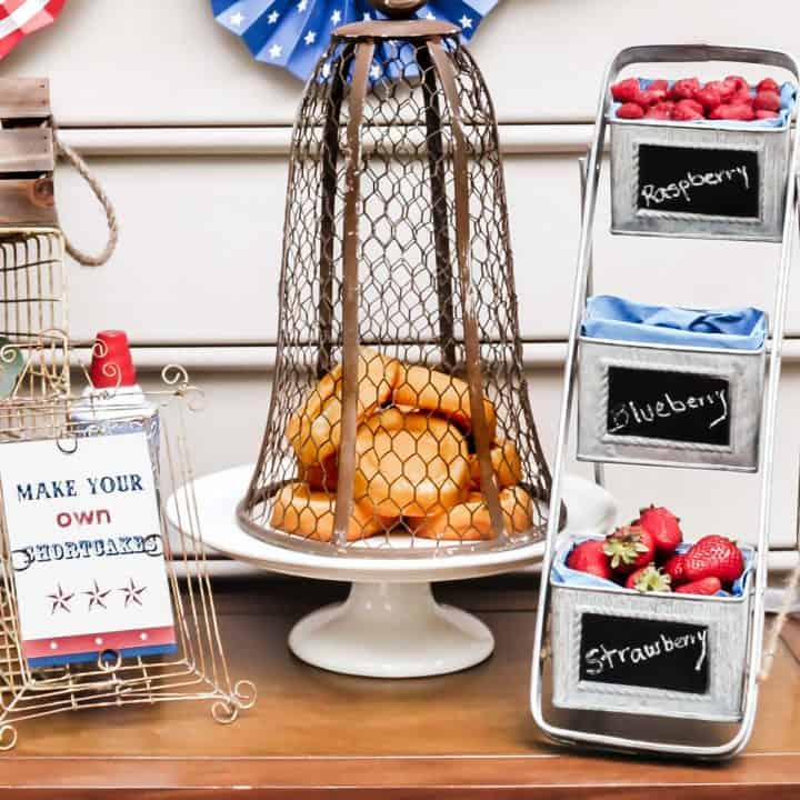 red, white, and blue decorations on table with little sponge cakes, fresh berries, and dessert table sign.