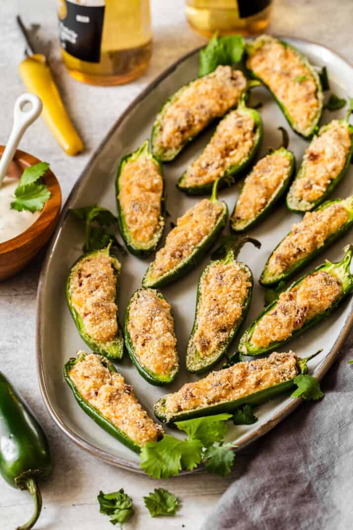 baked jalapeno poppers on gray platter surrounded by dip bowl and beer bottles.