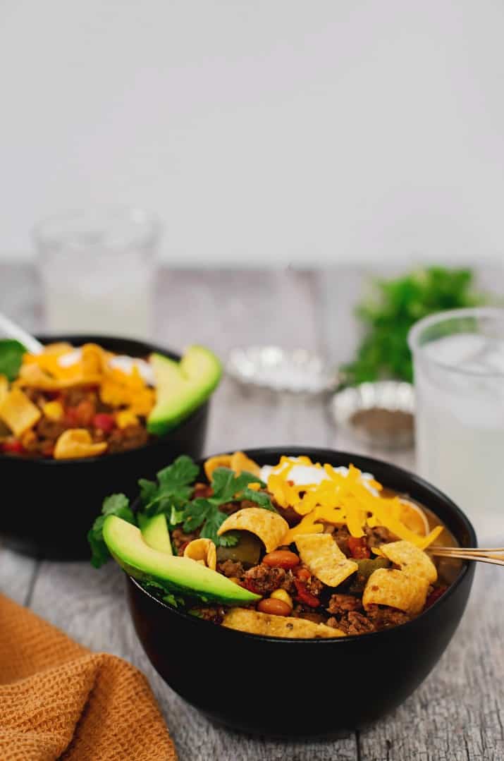 easy slow cooker fiesta chili recipe in two black bowls topped with fritos cheese and sour cream