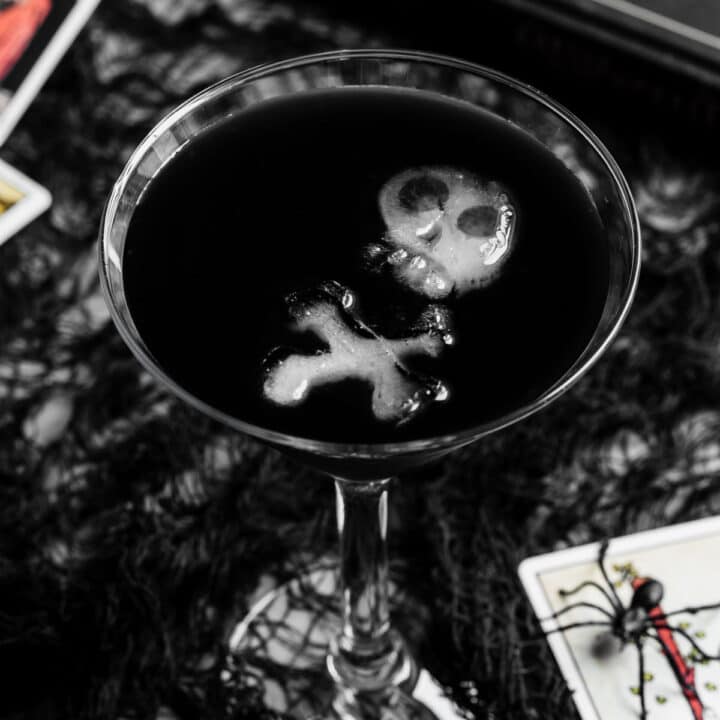 black Halloween drink in martini glass with skull shaped ice cubes.