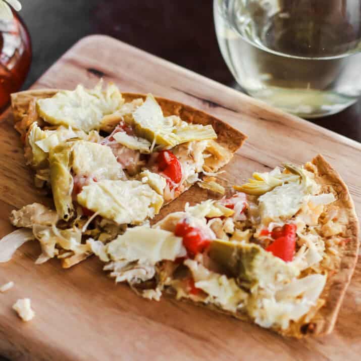 pizza slices with chicken, artichokes, and red peppers, on wood board.
