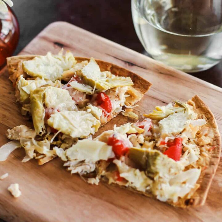 pizza slices with chicken, artichokes, and red peppers, on wood board.
