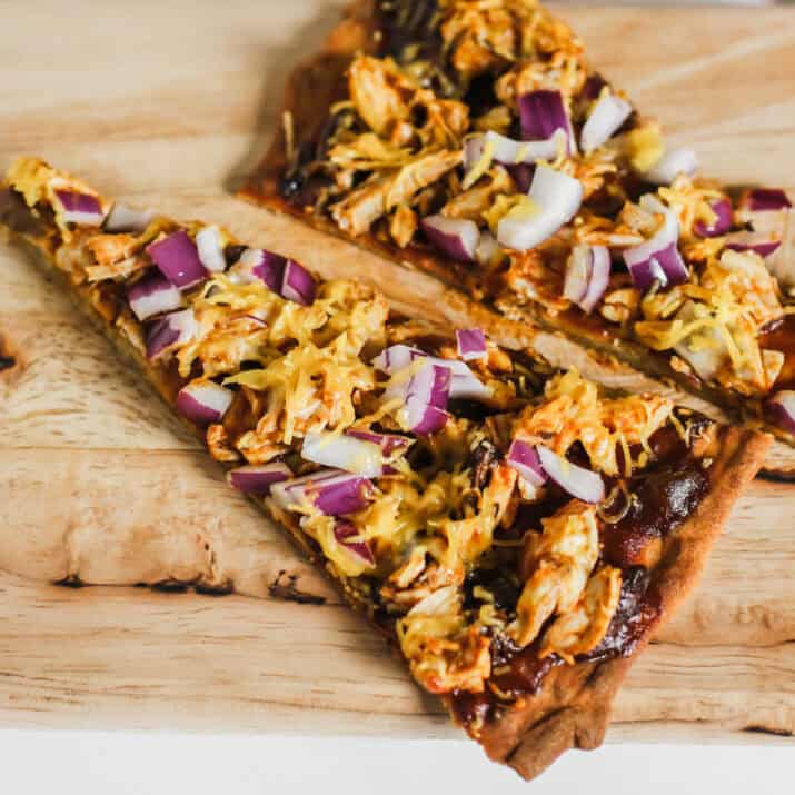 two slices of thin crust barbecue chicken pizza with cheddar and purple onions.