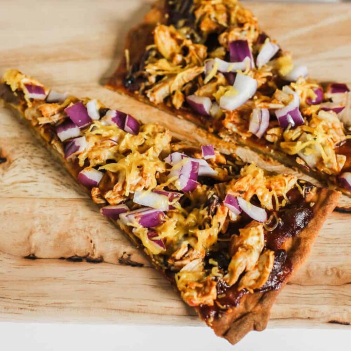 two slices of thin crust barbecue chicken pizza with cheddar and purple onions.