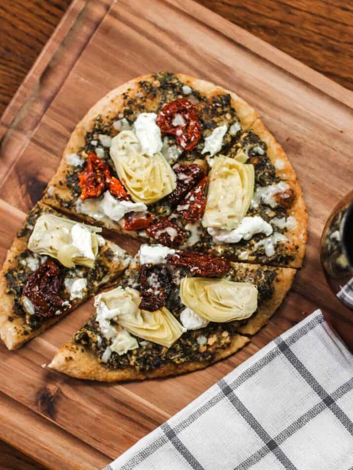 pizza on wood board, with artichokes, pesto, and sundried tomatoes.