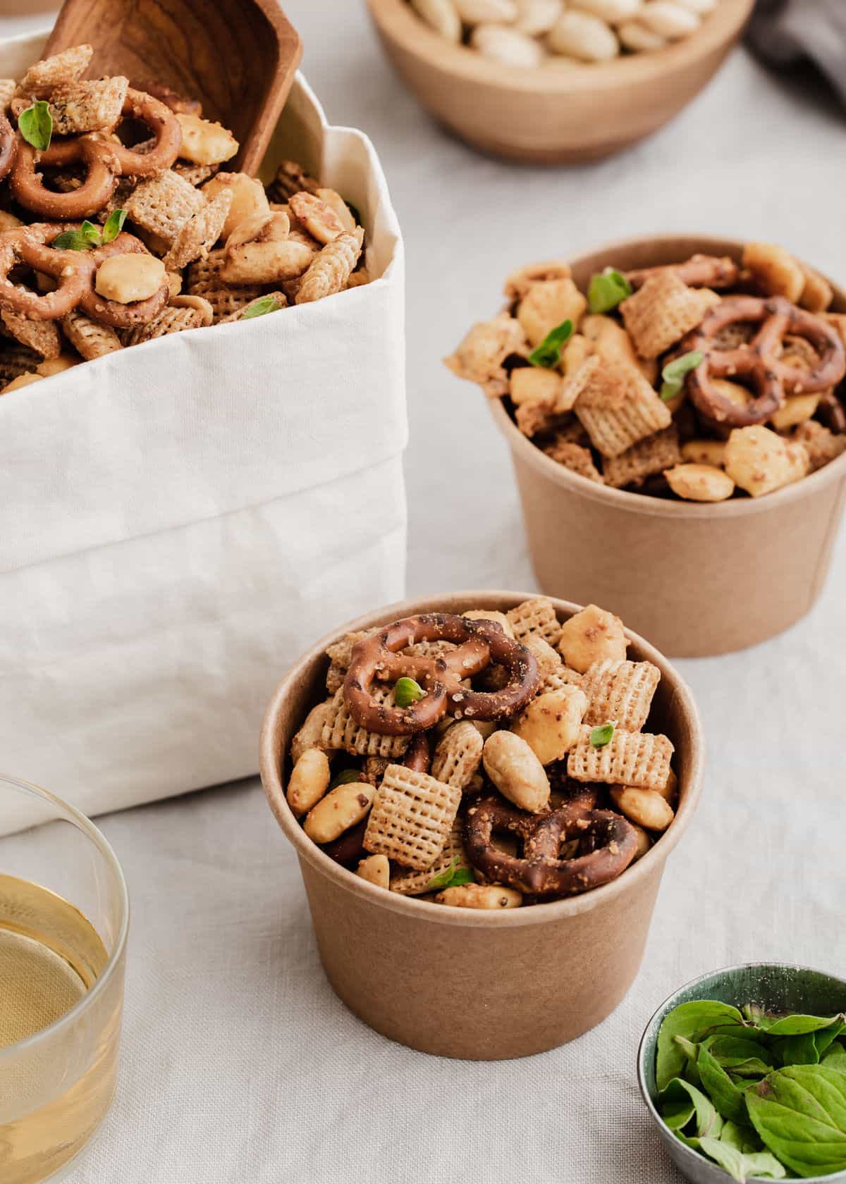 small brown snack cups filled with Chex mix on table with white bag full of more snack mix in background.