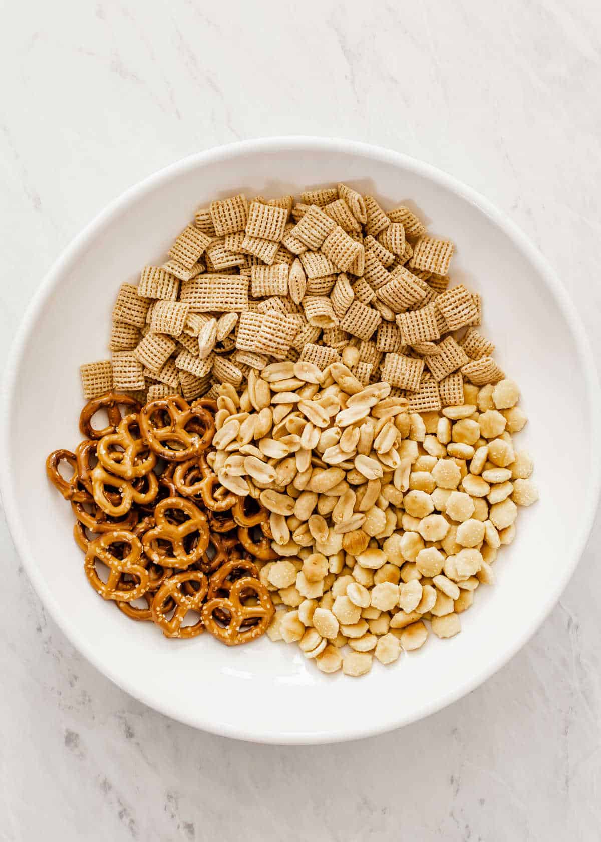 large white bowl filled with Corn Chex, mini pretzels, oyster crackers and peanuts.