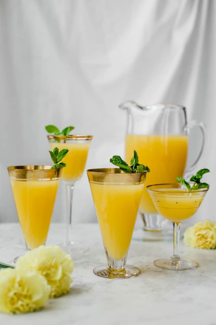 pitcher of yellow sparkling fruit punch in a variety of glasses