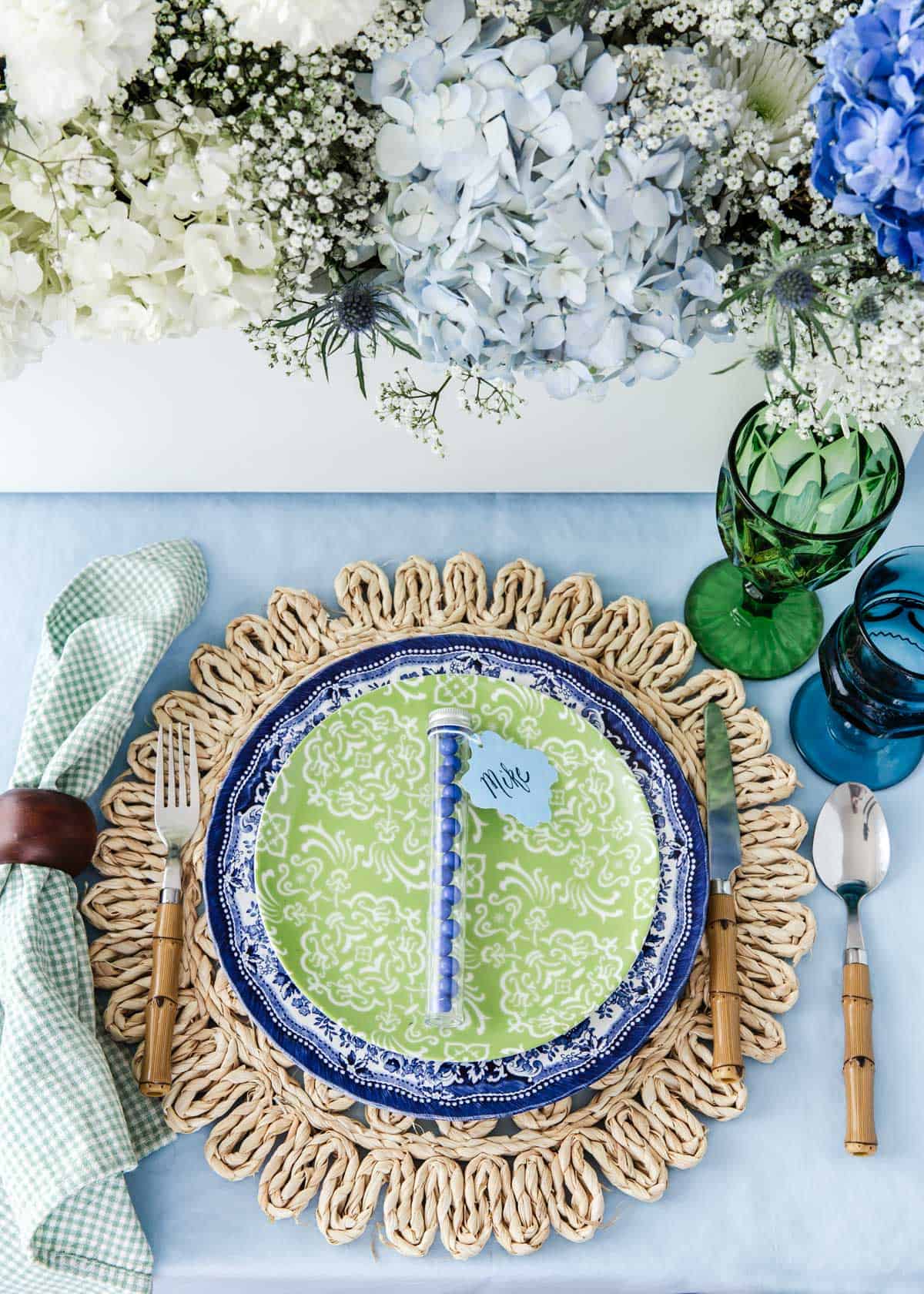 dinner table with woven place mat, blue dinner plate, green salad plate and blue and green glasses.