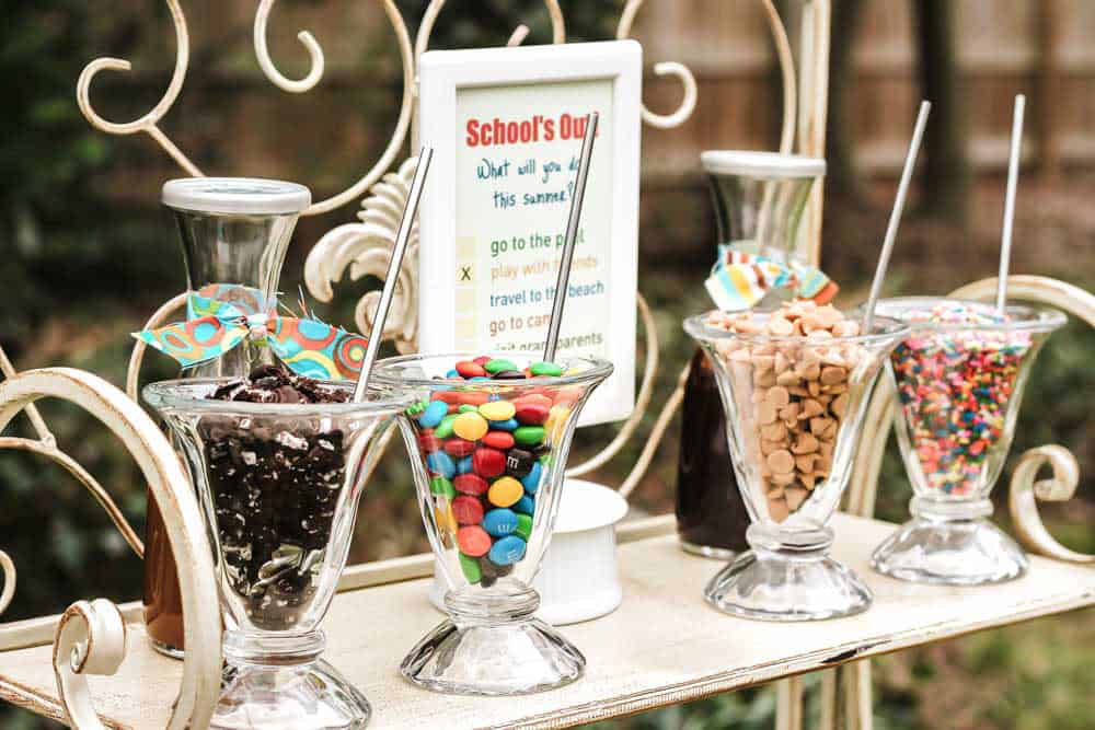 shelf set up outside with glass jars filled with sprinkles, crushed cookies, and syrups for ice cream sundaes. 
