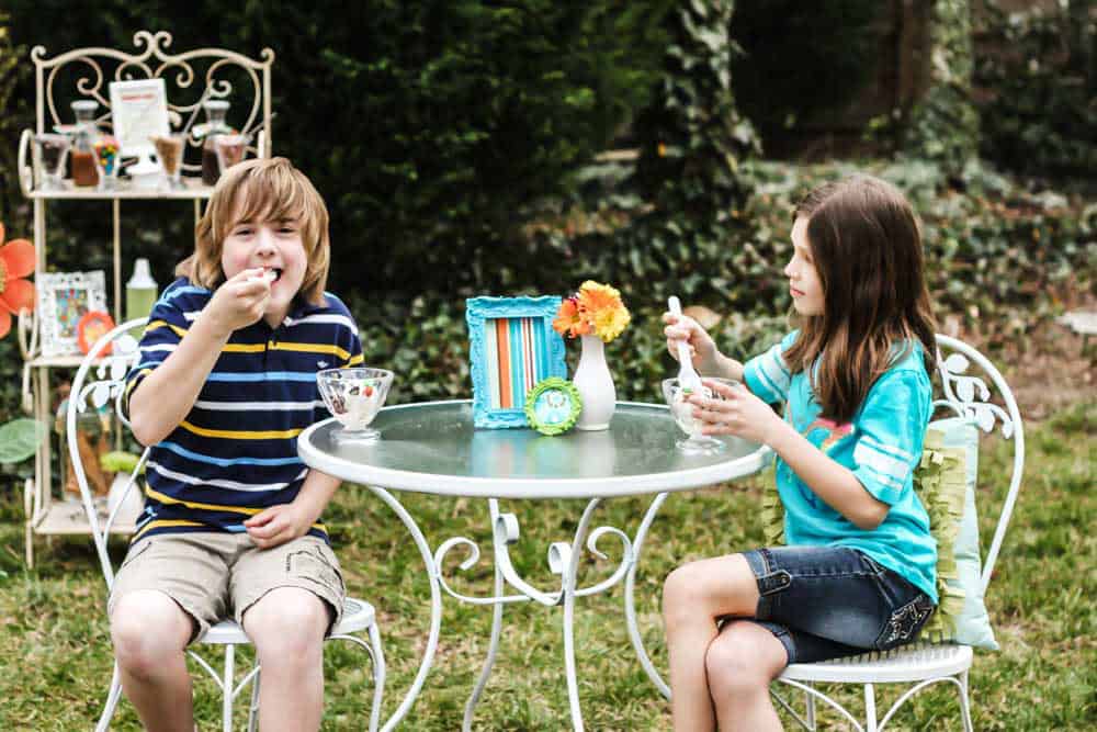 boy and girl sitting at bistro table outside, eating ice cream.