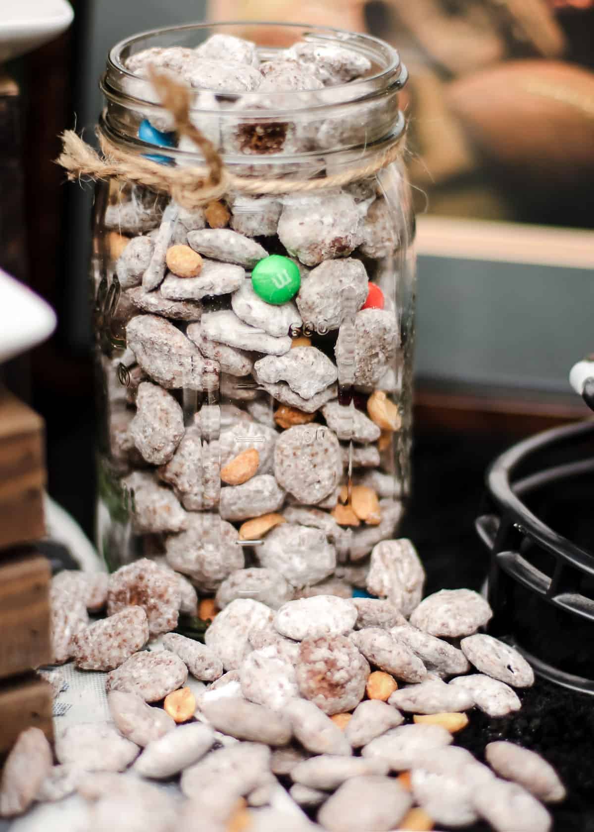 large mason jar with sweet puppy chow mix overflowing onto the table.