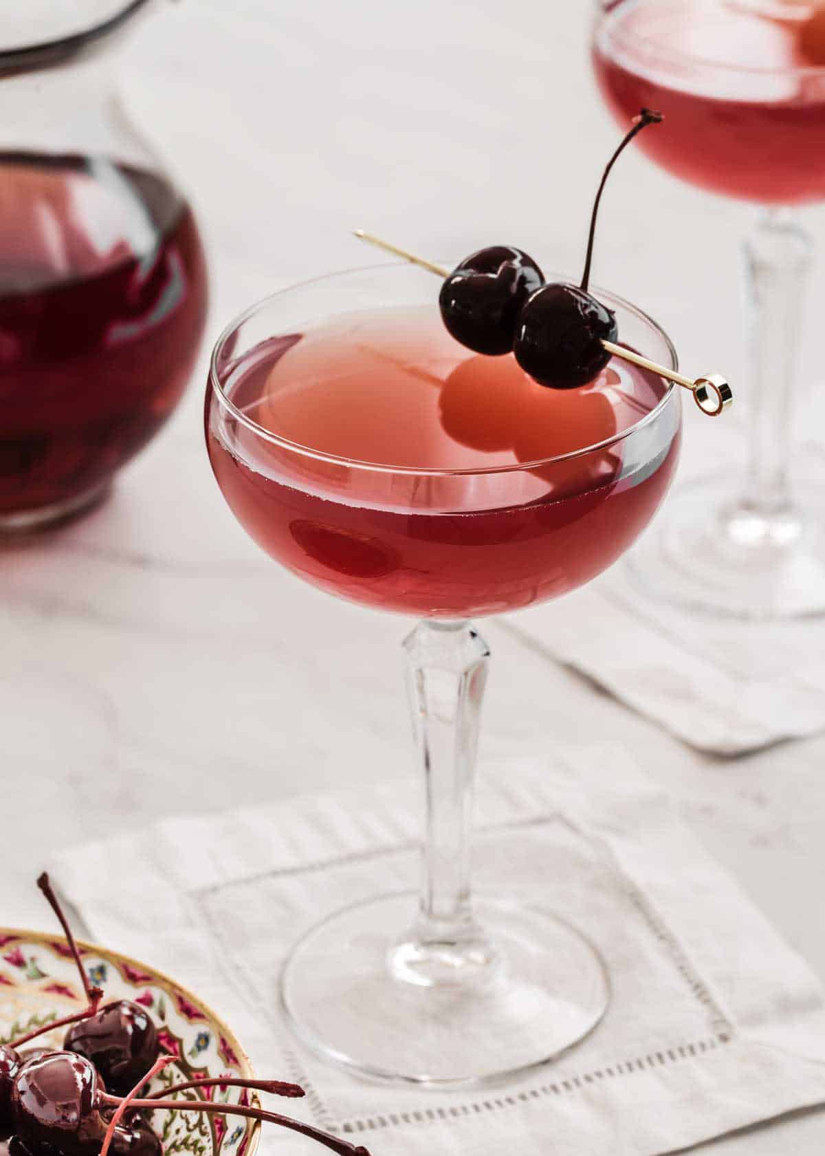 stem glass with red drink inside and cherry garnish.