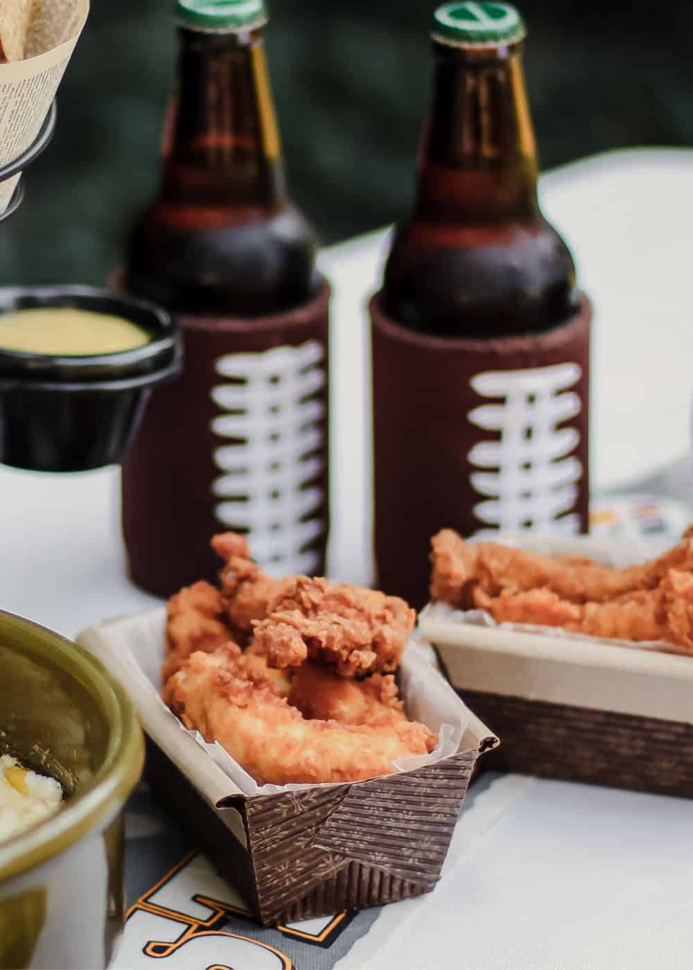 fried chicken fingers in disposable baskets with beer on outside table.