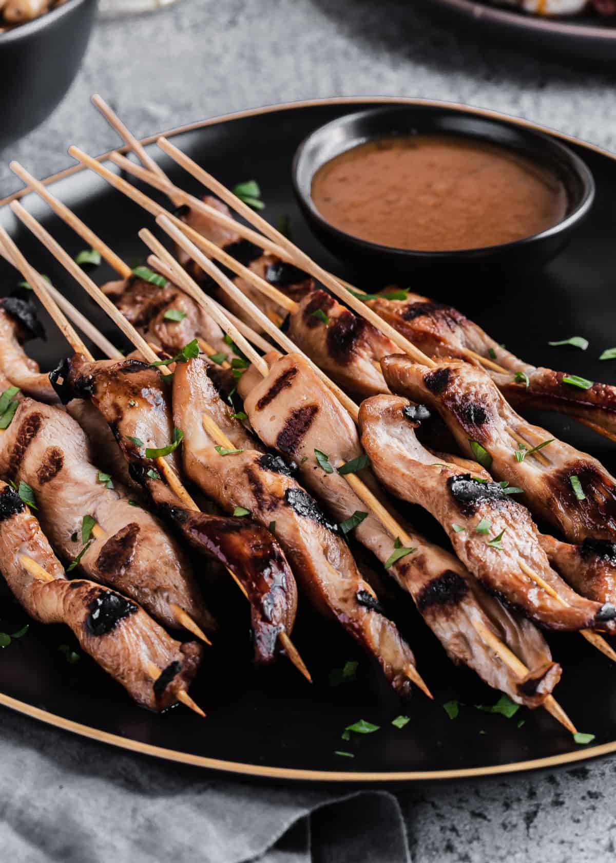 chicken on skewers with dipping sauce on black plate.