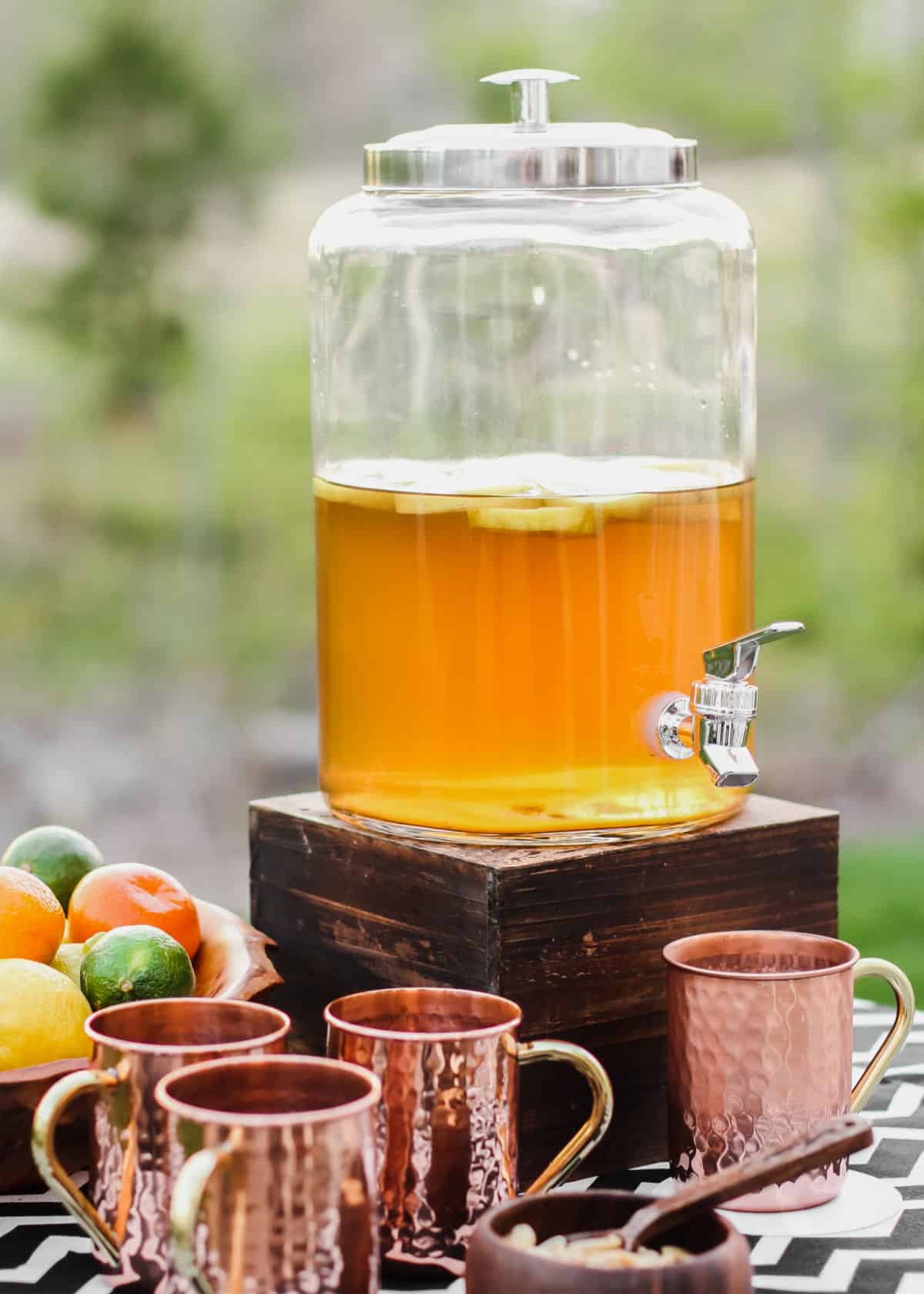 golden color punch in clear dispenser with copper cups.