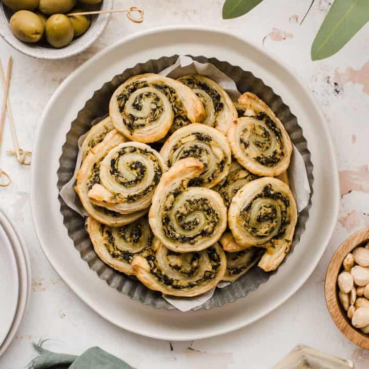 puff pastry pinwheel appetizers with spinach and artichoke filling, piled on plate.