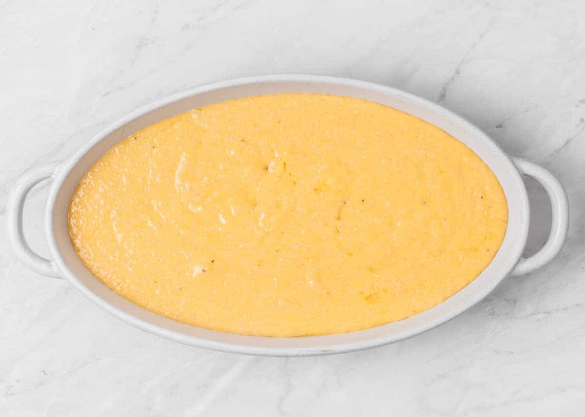prepared cheesy grits in dish before baking, on marble backdrop.