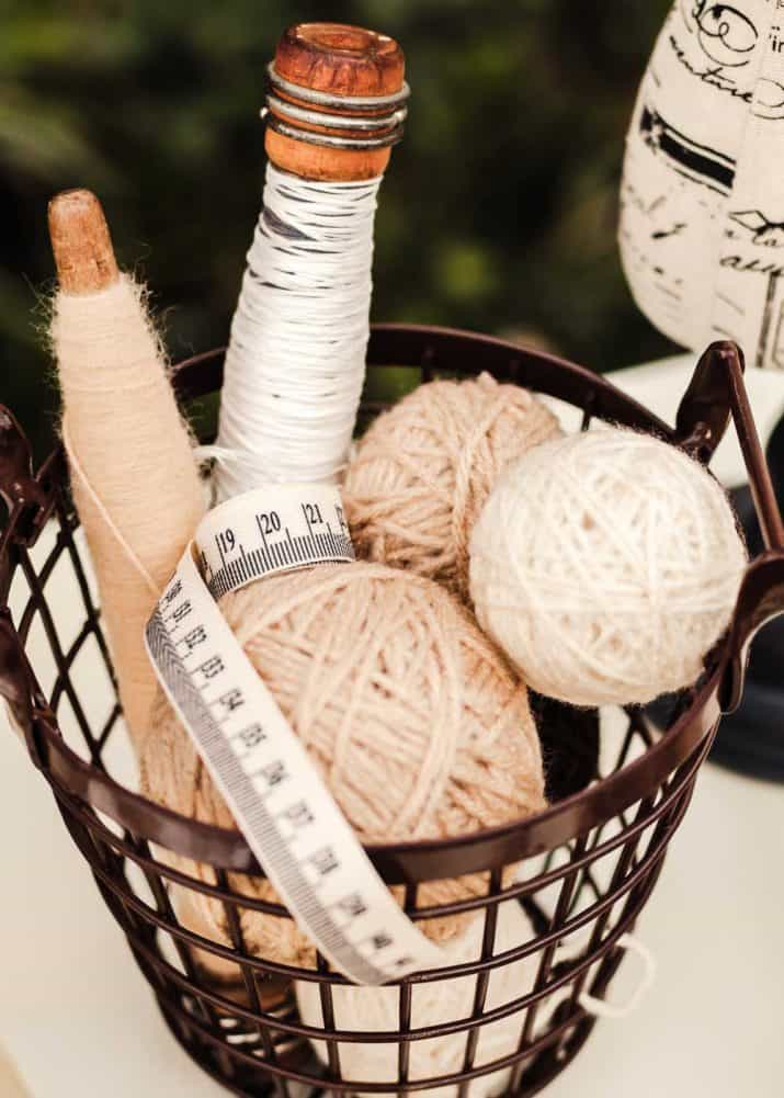small wire basket filled with yarn balls, vintage thread spools, and canvas measuring tape.