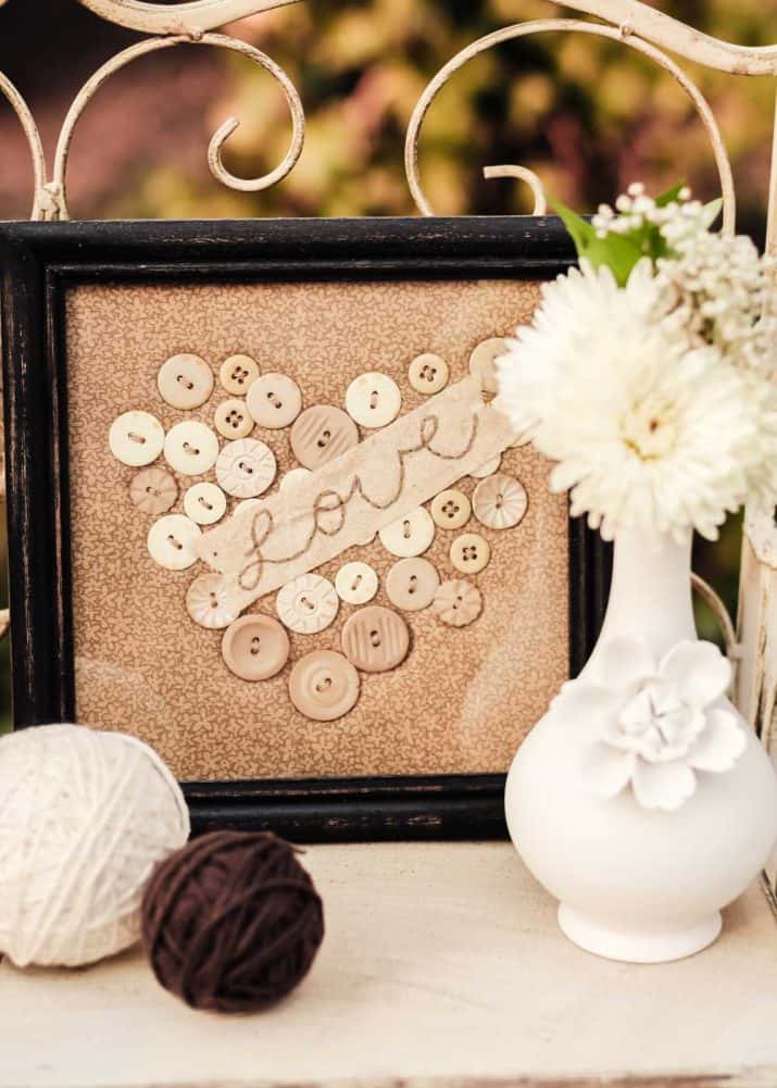 vintage style frame with fabric inside and buttons attached in the shape of a heart.