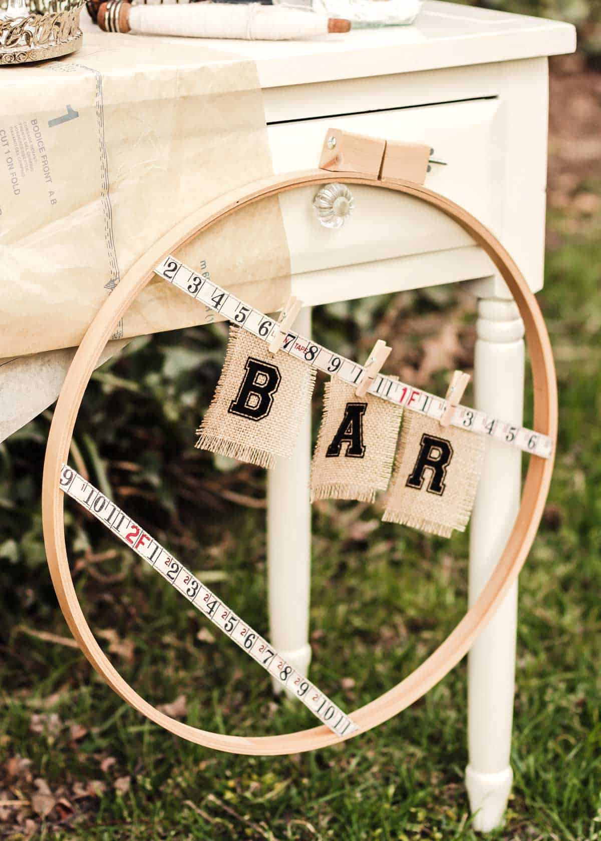 large embroidery hoop with DIY bar sign hung on it.