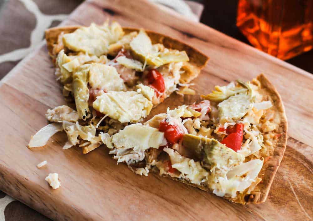 thin crust pizza slices with chicken and artichokes, on wood board.