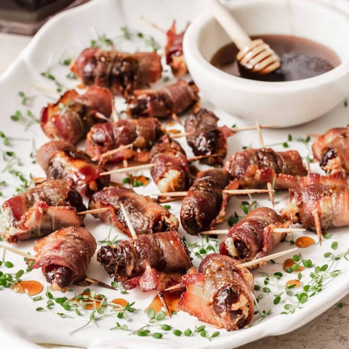 bacon wrapped dates appetizers on white platter with small bowl of honey with honey stick.