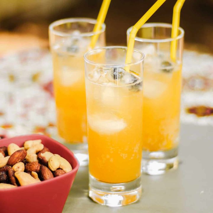 three glasses filled with orange drink and straws.
