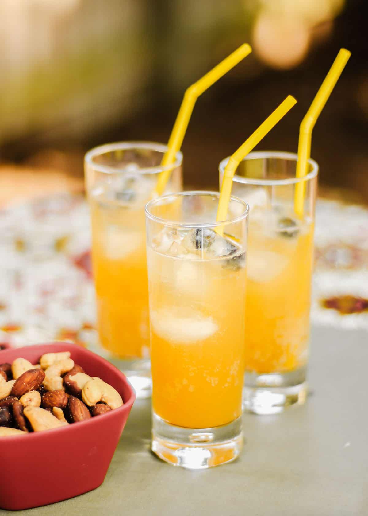 three glasses filled with orange drink with straws, in outdoor setting.